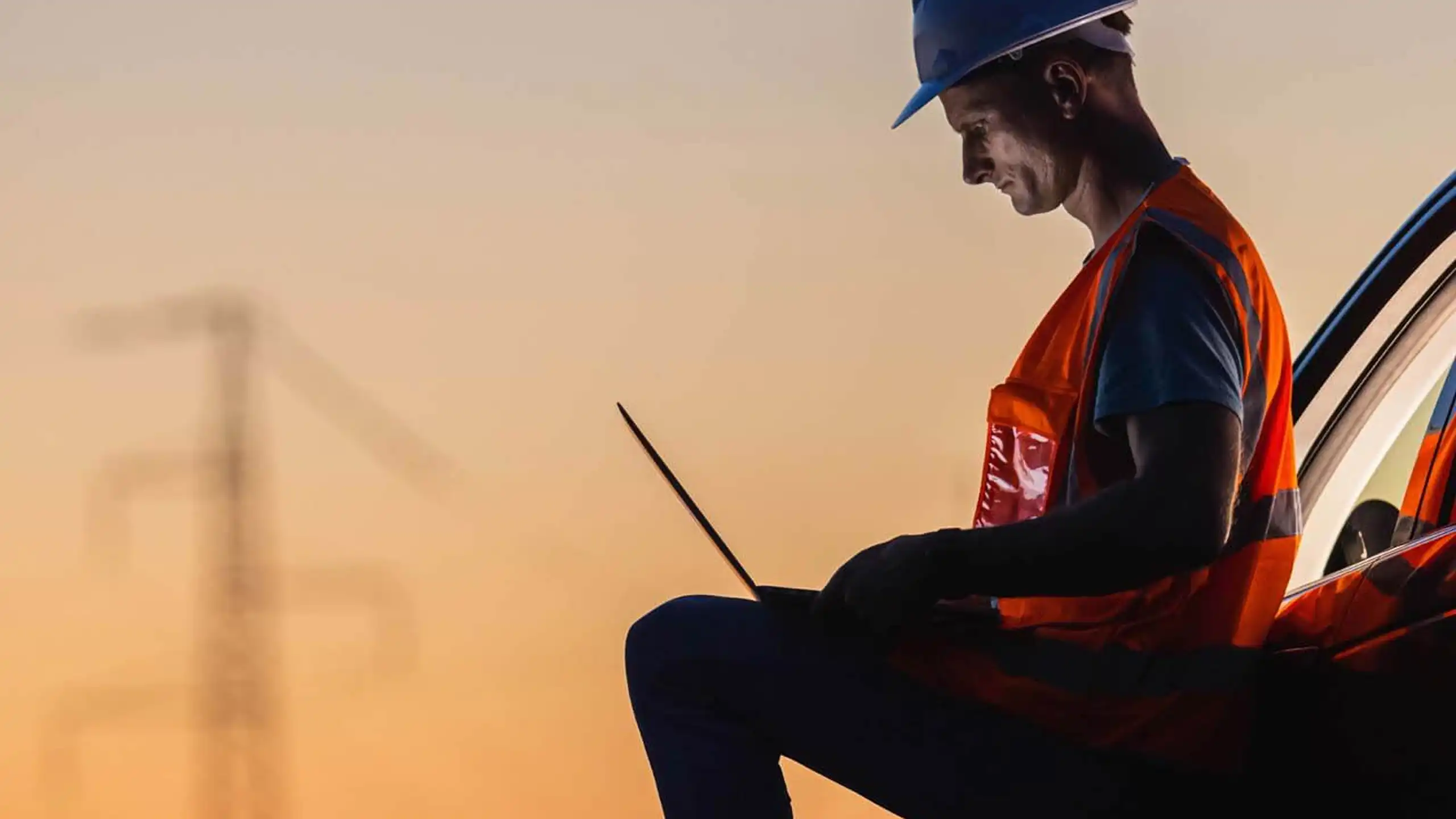 Energy engineer working at a laptop beside a vehicle at sunset.