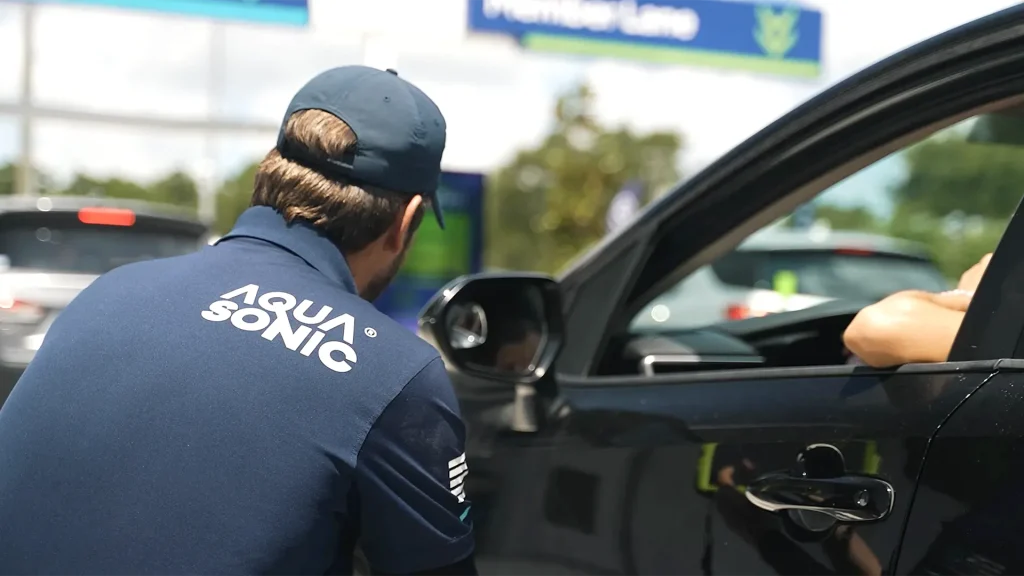 AquaSonic team member assisting a customer during the drive-thru check-in process at an AquaSonic car wash location.